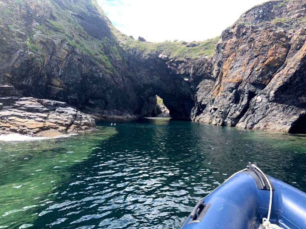 Small boat exploring the sea caves and granite cliffs at Kynance Cove in Cornwall.