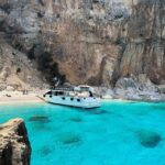 Boat anchored in the turquoise waters of Cala Luna in Sardinia's Golfo di Orosei, accessible only by boat or hiking trail.