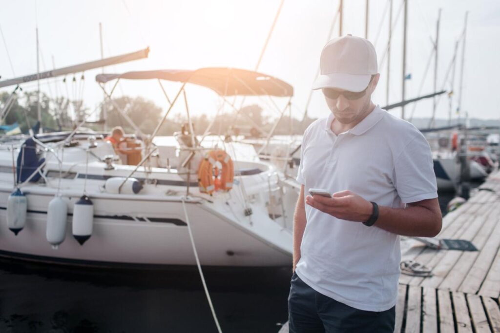 Boat owner creating an online listing for a charter boat using a smartphone at the marina.