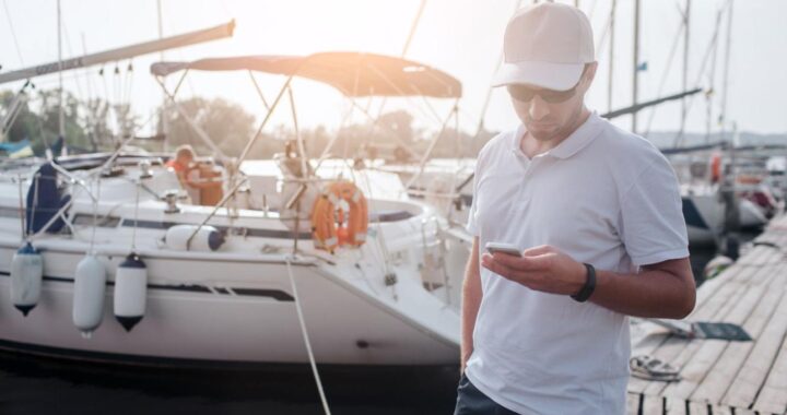 Boat owner creating an online listing for a charter boat using a smartphone at the marina.