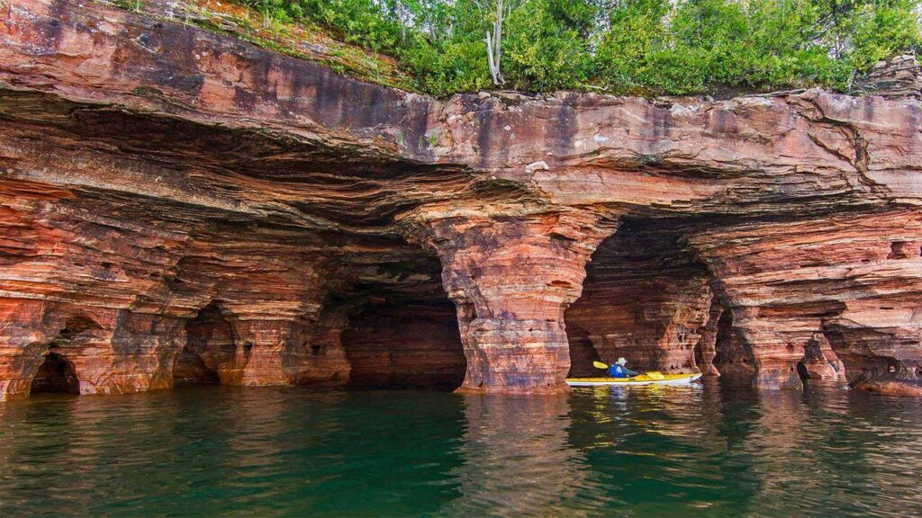 Kayakers entering the famous sandstone sea caves of the Apostle Islands on Lake Superior, one of America's most spectacular hidden water adventures.