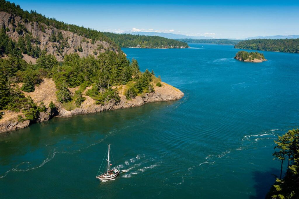 Sailboat navigating the San Juan Islands in Washington State surrounded by forested islands.