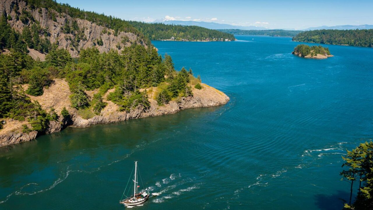 Sailboat navigating the San Juan Islands in Washington State surrounded by forested islands.