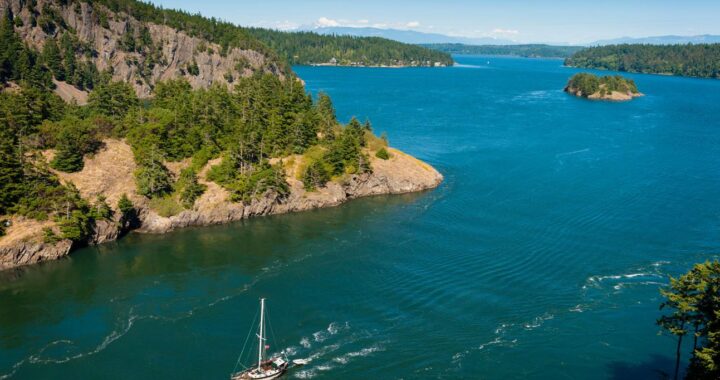 Sailboat navigating the San Juan Islands in Washington State surrounded by forested islands.