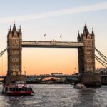 Tower Bridge viewed from a boat cruising along the River Thames at sunset.