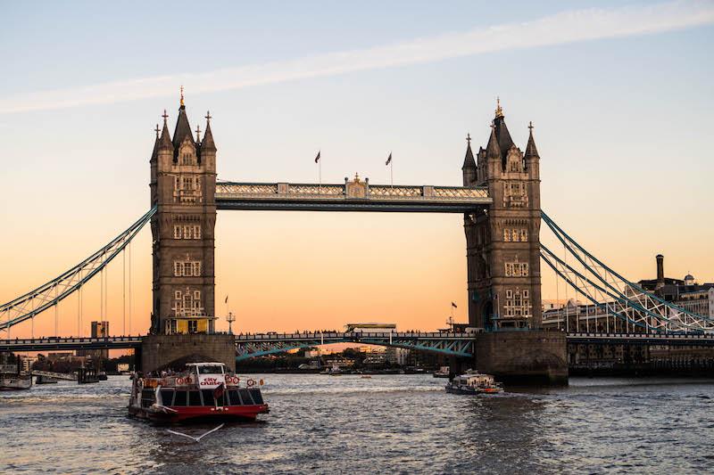 Tower Bridge viewed from a boat cruising along the River Thames at sunset.