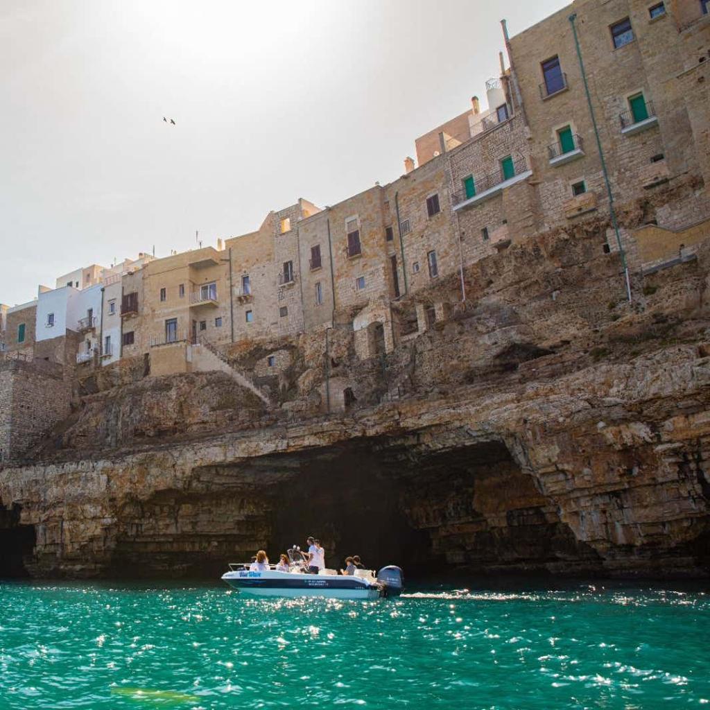 Small boat exploring the limestone sea caves of Polignano a Mare on Italy's Adriatic coast.