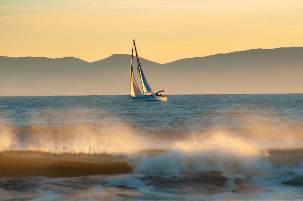 Sailing yacht cruising along the California coast at sunset.